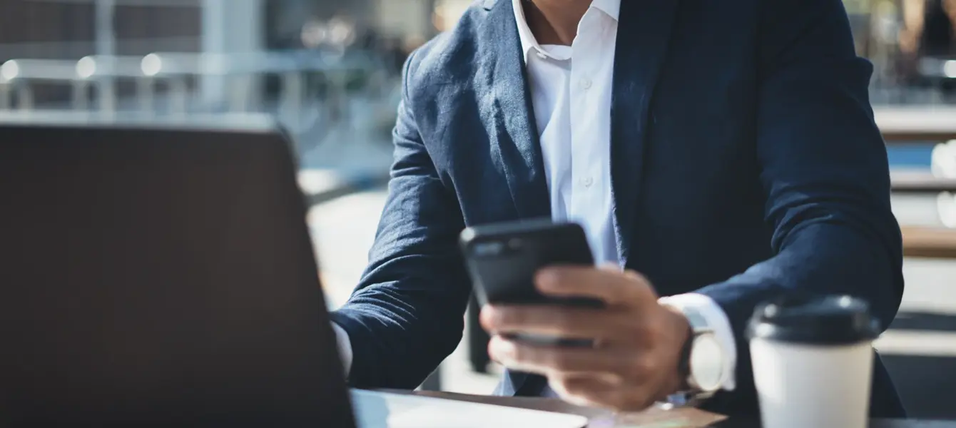 Homem de fato a usar telemóvel com portátil e café na mesa