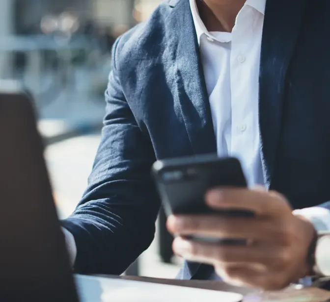 Homem de fato a usar telemóvel com portátil e café na mesa