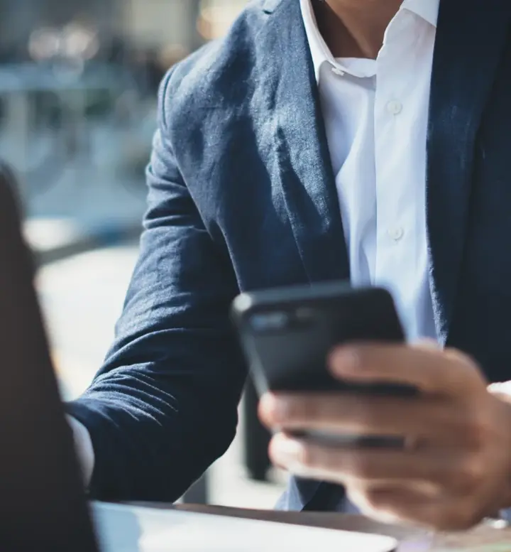Homem de fato a usar telemóvel com portátil e café na mesa