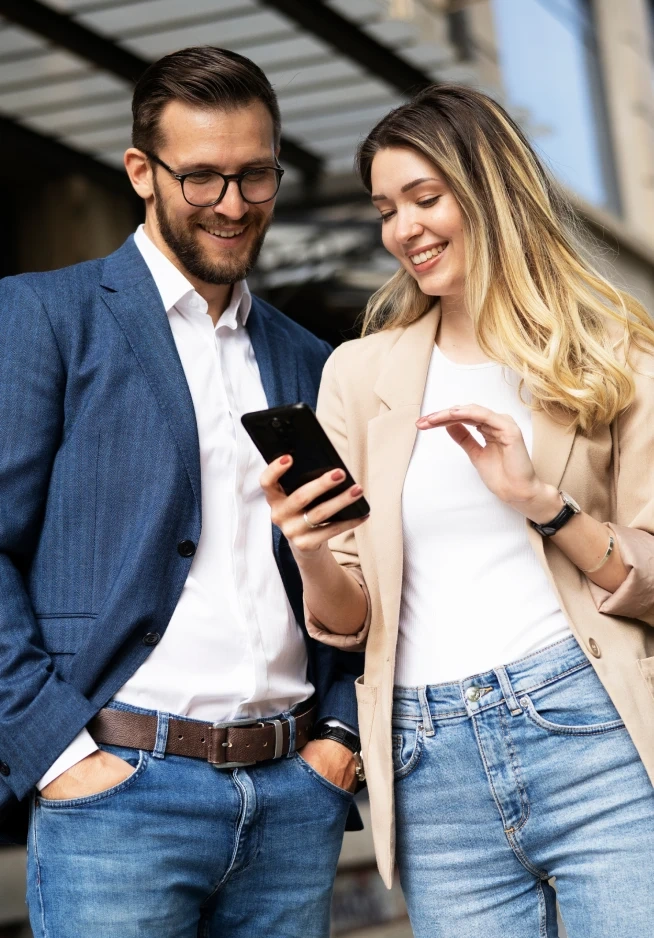 Homem e mulher sorriem enquanto olham para o ecrã de um telemóvel
