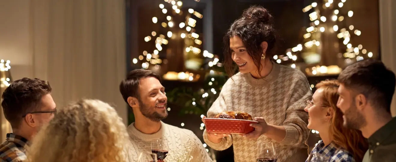 Mulher serve um prato a amigos durante um jantar festivo