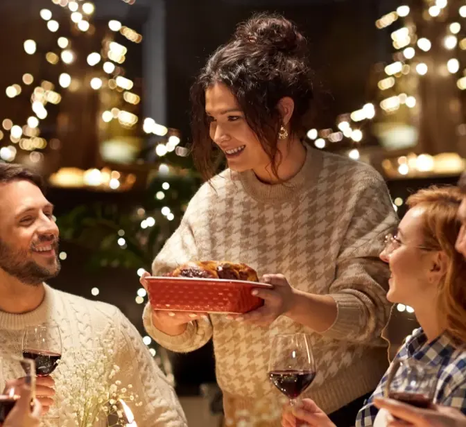 Mulher serve um prato a amigos durante um jantar festivo