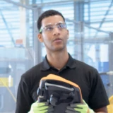 man in a factory, operating a machine with a remote control