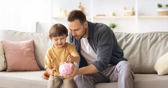 Pai e filho a colocar moedas num mealheiro rosa no sofá