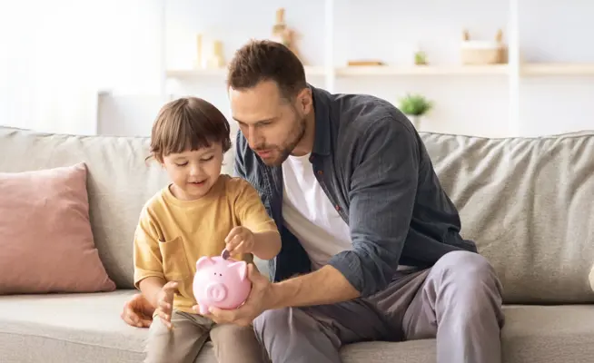 Pai e filho a colocar moedas num mealheiro rosa no sofá