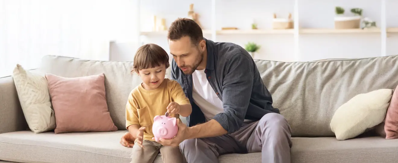 Pai e filho a colocar moedas num mealheiro rosa no sofá
