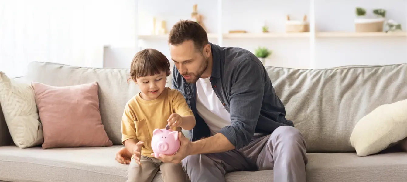 Pai e filho a colocar moedas num mealheiro rosa no sofá