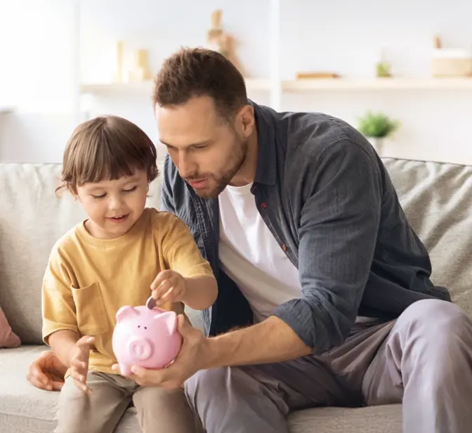 Pai e filho a colocar moedas num mealheiro rosa no sofá