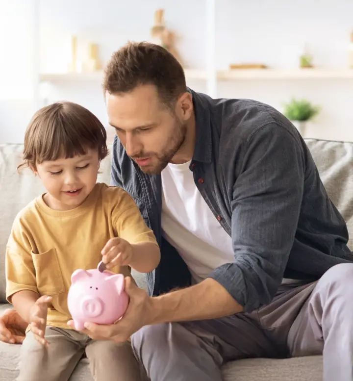 Pai e filho a colocar moedas num mealheiro rosa no sofá