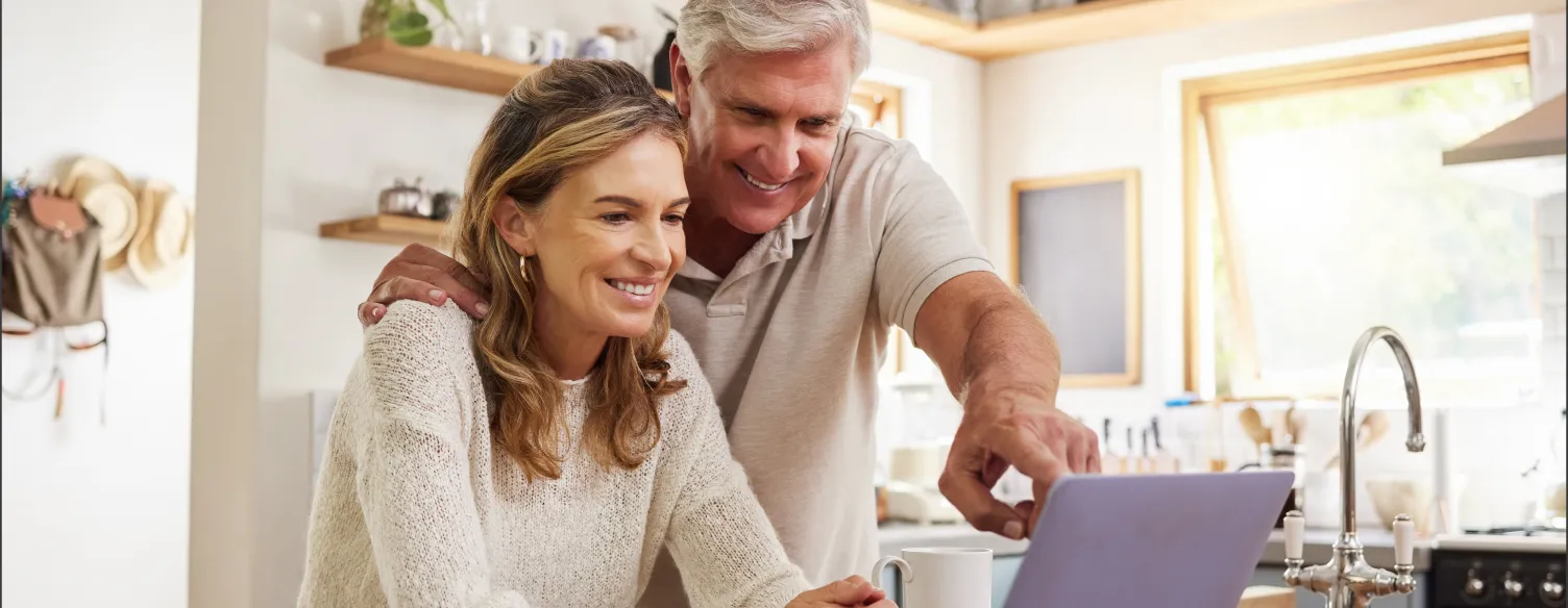 casal sorridente, na cozinha, a mexer num pc portátil