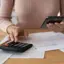 Mulher usa calculadora e telemóvel para organizar contas numa secretária de madeira