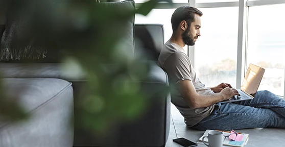 man sitting on the floor, leaning against the sofa, with a laptop