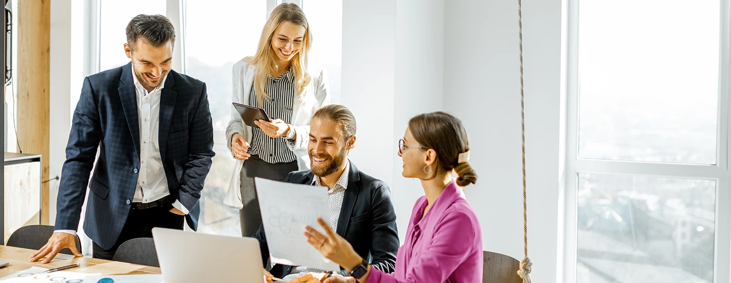 4 pessoas numa sala de reuniões, com computador e portátil, sorridentes