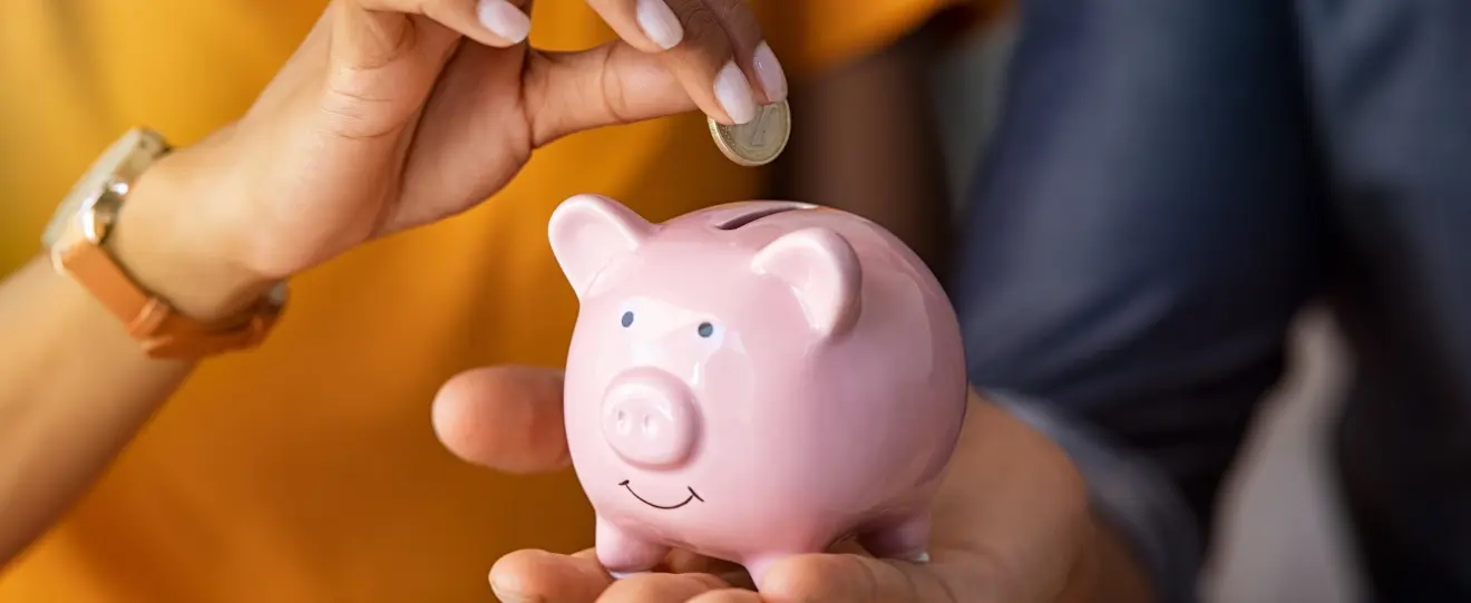 Mãos a colocar uma moeda num mealheiro rosa