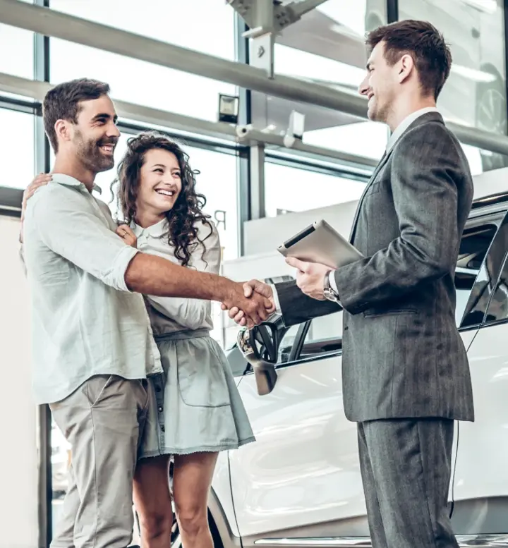 Casal a apertar a mão a vendedor de carros numa concessionária