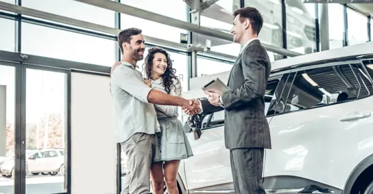 Casal a apertar a mão a vendedor de carros numa concessionária