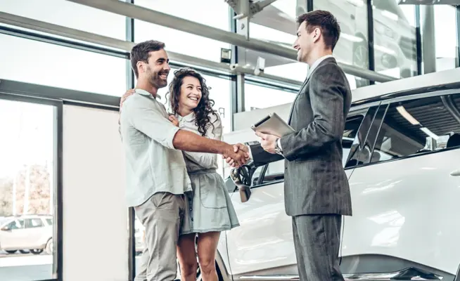 Casal a apertar a mão a vendedor de carros numa concessionária