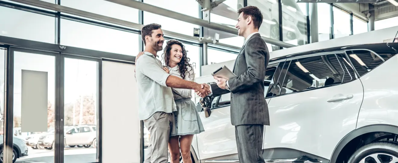 Casal a apertar a mão a vendedor de carros numa concessionária