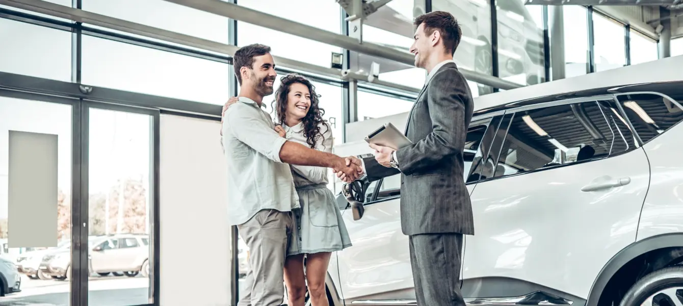 Casal a apertar a mão a vendedor de carros numa concessionária