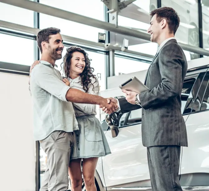Casal a apertar a mão a vendedor de carros numa concessionária
