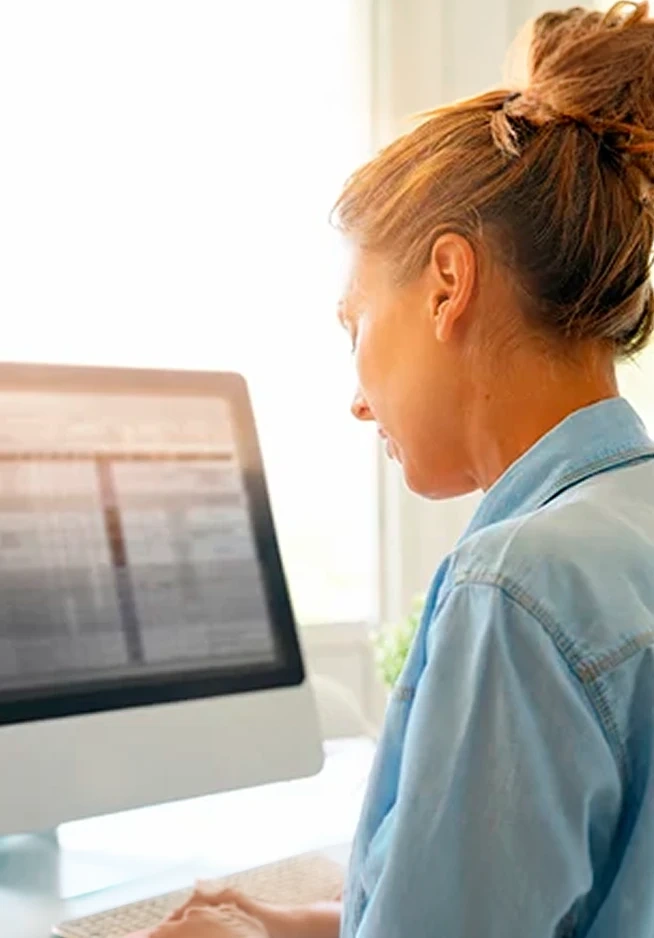 Mulher de costas a trabalhar num computador de secretária