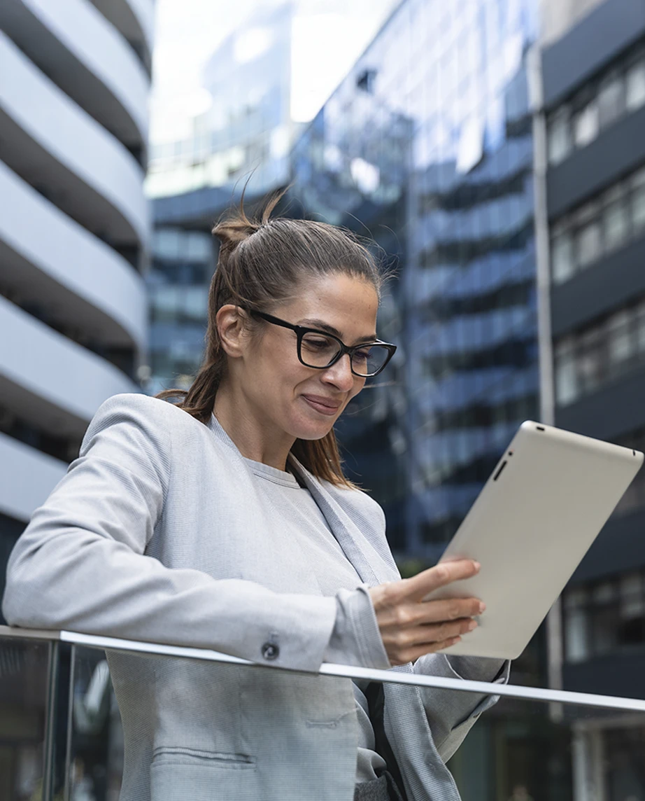 senhora sorridente com tablet, no terraço de um prédio numa cidade