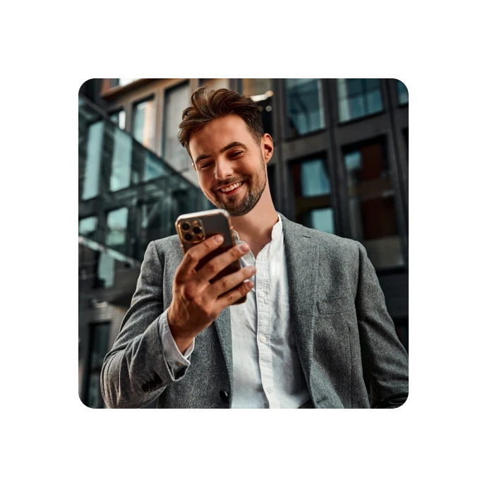 jovem sorridente, vestido formalmente, a olhar para telemóvel