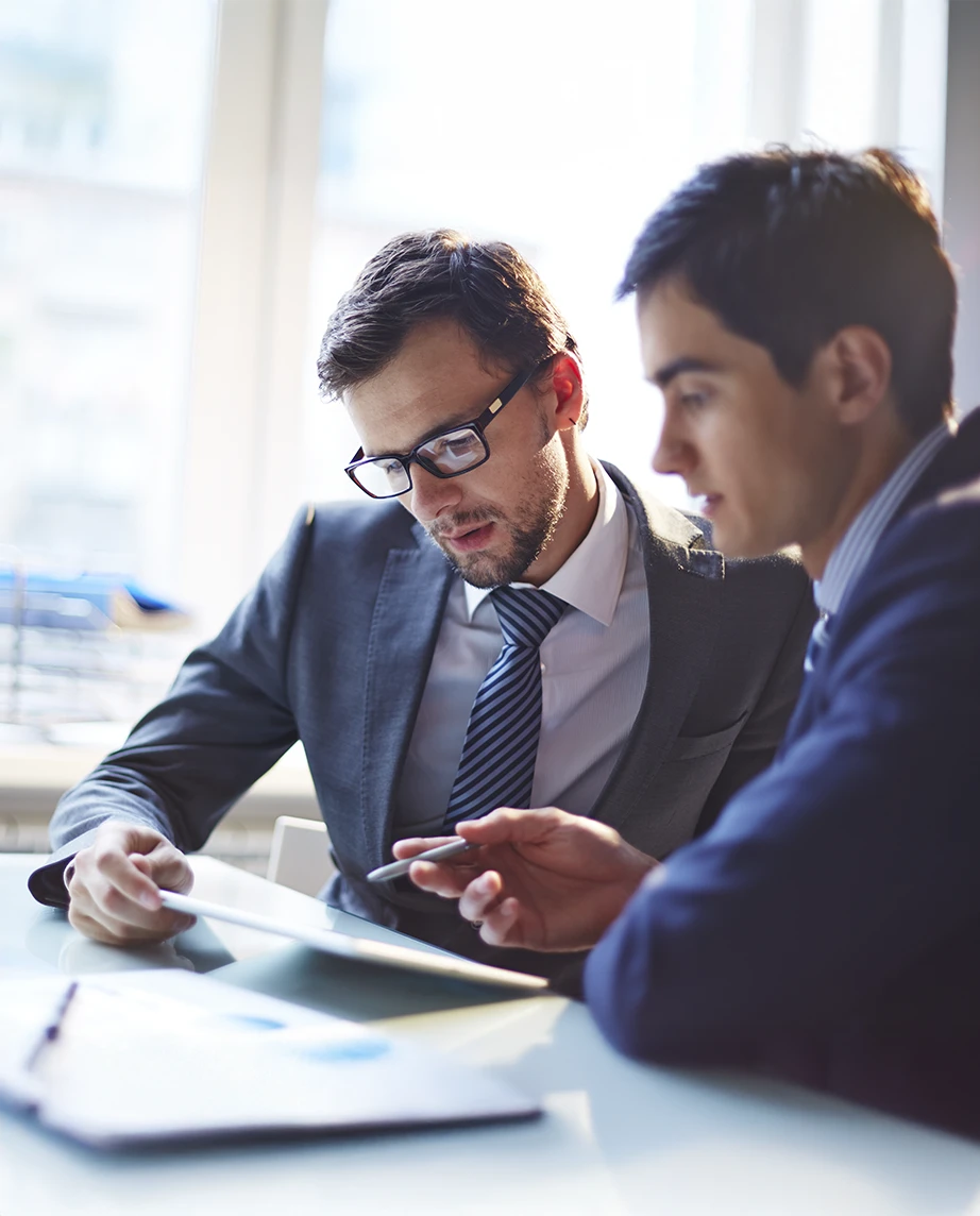 2 homens vestidos formalmente, numa reunião, com papéis