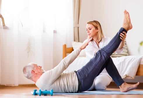 senhor a fazer fisioterapia em casa, com ajuda de uma fisioterapeuta