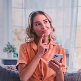  A smiling woman, looking amused and thoughtful, with a mobile phone in her hand