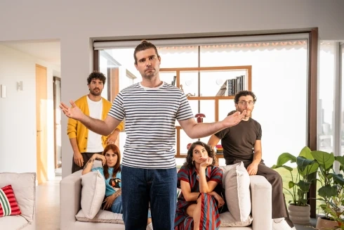 Filipe Ribeiro de braços abertos em frente a um grupo de amigos com ar aborrecido no sofá