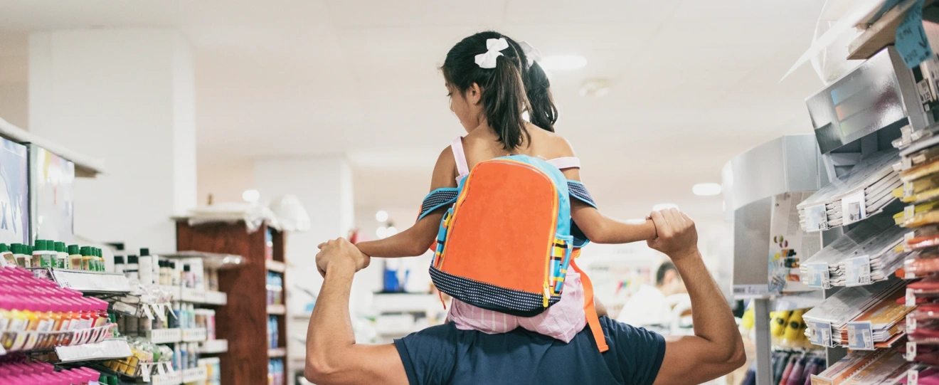 Pai com filha aos ombros a escolher material escolar numa papelaria