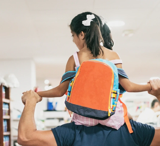 Pai com filha aos ombros a escolher material escolar numa papelaria