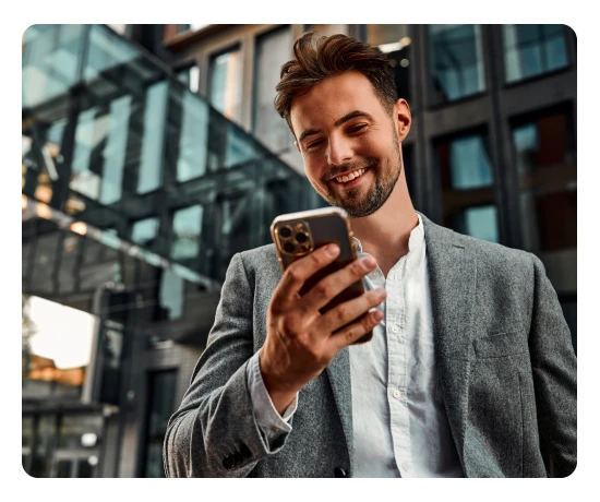 Homem sorri enquanto usa smartphone numa rua urbana