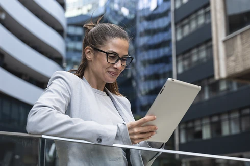 senhora sorridente com tablet, no terraço de um prédio numa cidade