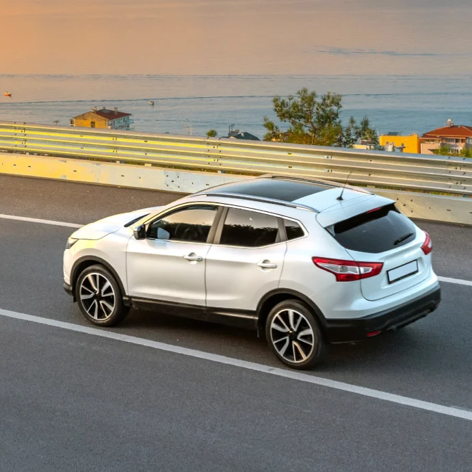 Carro branco numa estrada com rails de proteção e vista rio