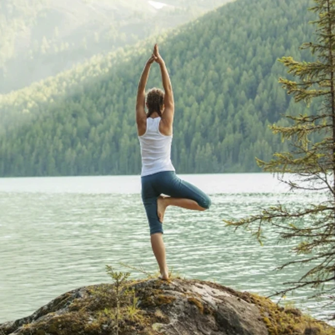 Woman posing in a yoga position on a rock in front of a river and mountains