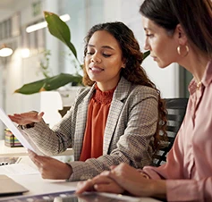 2  mulheres num escritório, uma com papel na mão, a conversar