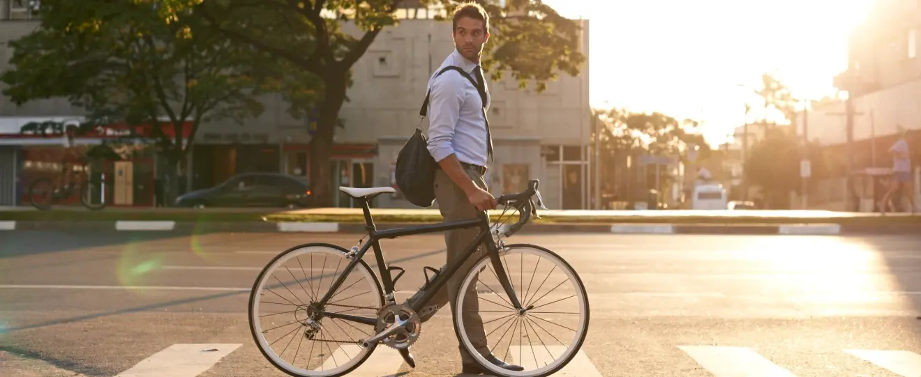 Homem de fato a atravessar passadeira com bicicleta ao pôr do sol