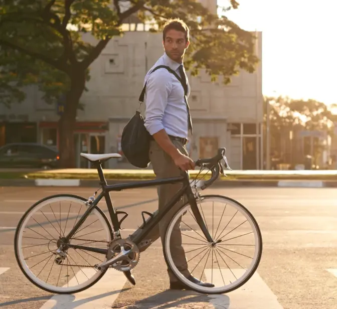 Homem de fato a atravessar passadeira com bicicleta ao pôr do sol