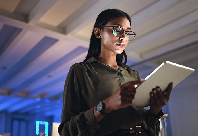 Mulher de óculos a utilizar um tablet num ambiente com pouca luz