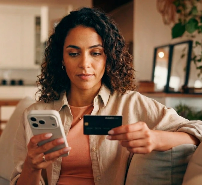 Mulher no sofá a usar o telemóvel e um cartão de crédito para um pagamento