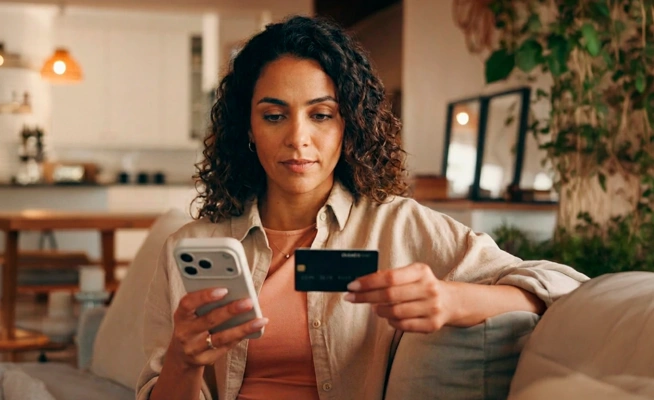 Mulher no sofá a usar o telemóvel e um cartão de crédito para um pagamento