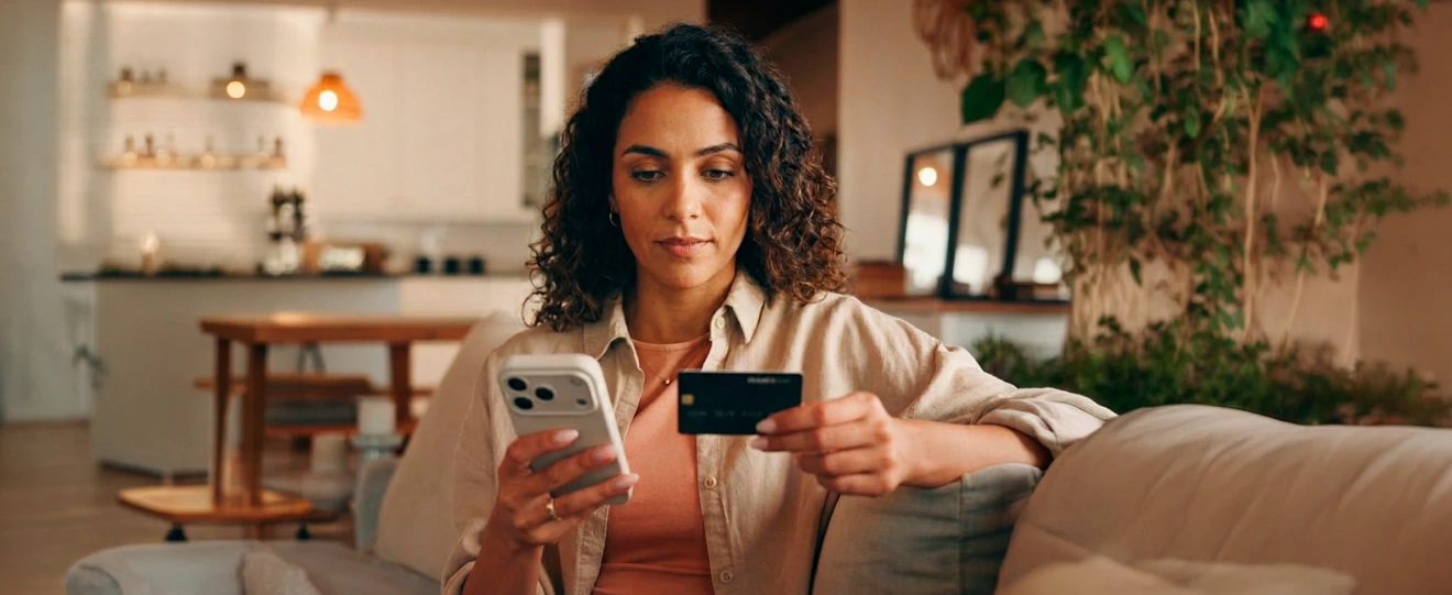 Mulher no sofá a usar o telemóvel e um cartão de crédito para um pagamento