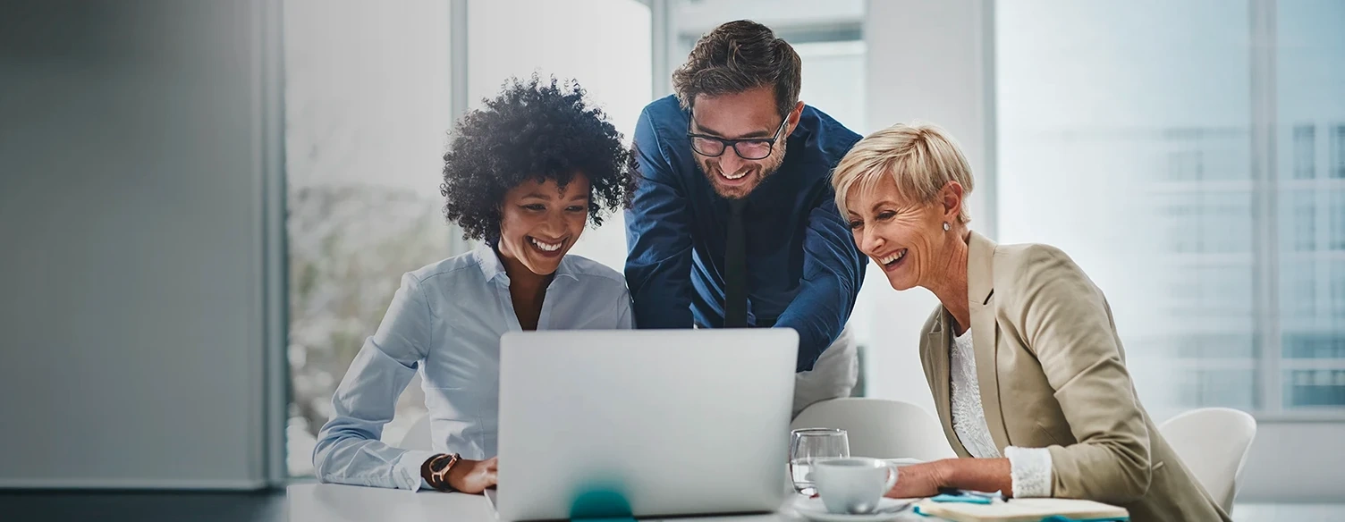 Três colegas de trabalho sorridentes a olhar para um ecrã de portátil num escritório