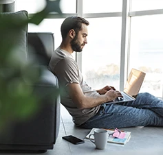 man sitting on the floor, leaning against the sofa, with a laptop