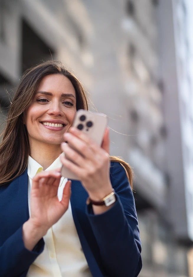 Woman in a suit smiles while using her mobile phone outdoors
