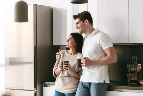 jovem casal segurando canecas, encostado ao balcão da cozinha