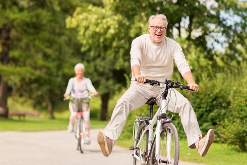 casal a andar de bicicleta, com ar divertido, num caminho de um parque verde