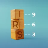 três dados de madeira, uns em cima dos outros, cada um com uma letra do "IRS"